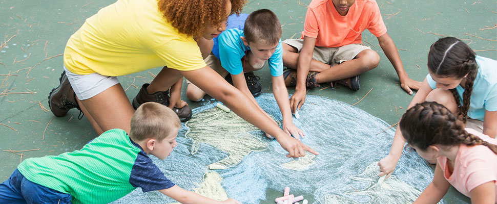 a group of children and a guardian making chalk art on a sidewalk