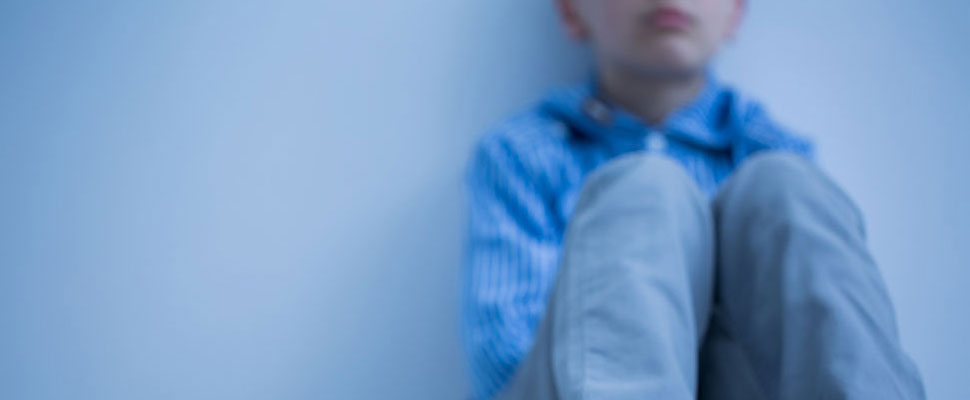 image of a boy sitting against a wall looking very sad