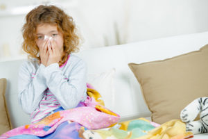 little girl blowing her nose while sitting on the couch